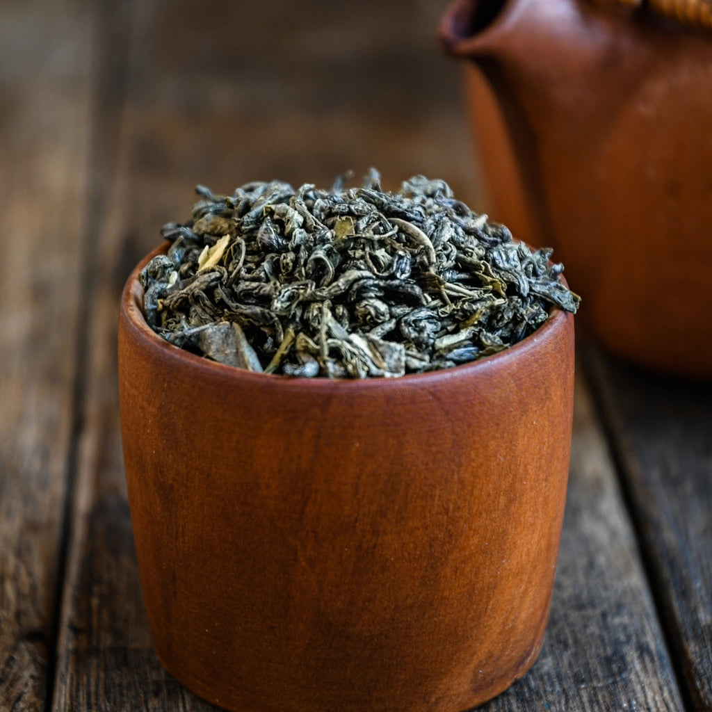 Dried tea leaves in a small wooden container on a wooden surface